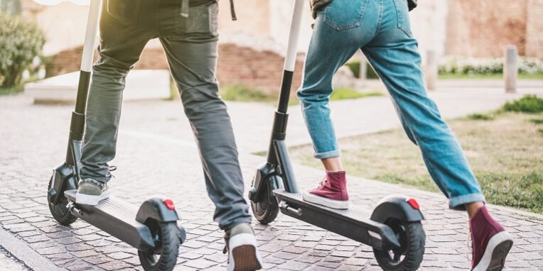 Close up of people couple using electric scooter in city park –